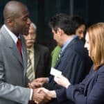 a male sales pro hands a business professional woman an business card at a networking event as a prospecting activity